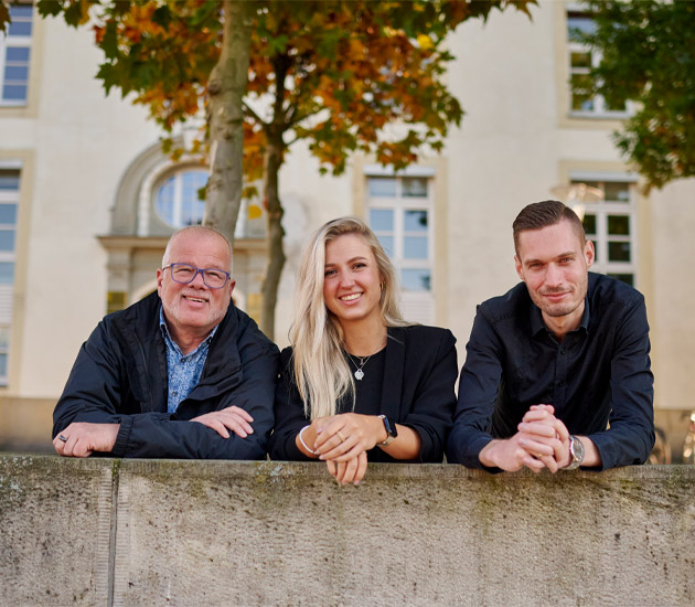 Drei Personen stehen an einer Mauer