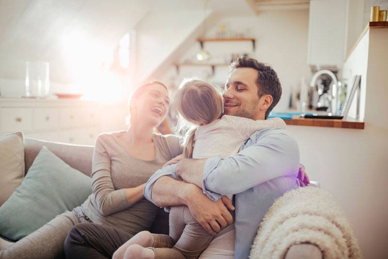Familie sitzt auf der Couch und er Vater hält das Kind im Arm